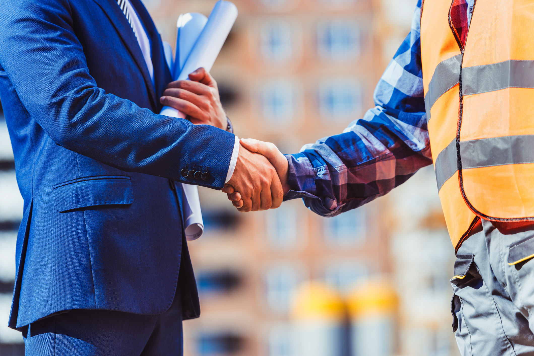 Cropped shot of construction worker in reflective vest shaking hands with businessman